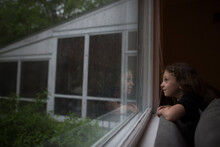 Side View Of Smiling Girl Looking Through Wet Window At Home During Rainy Season