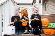 Playful Siblings In Halloween Costumes Sitting On Steps Against House
