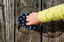 Cropped Hand Of Girl Picking Blueberries From Bowl On Wooden Table