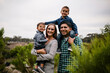 © Cavan Images - Portrait of happy parents carrying sons while standing by plants against sky at park