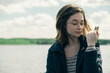© Cavan Images - Woman holding butterfly while sitting by lake against cloudy sky