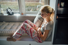 Side View Of Thoughtful Girl Sitting On Alcove Window Seat At Home