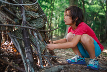 Boy Making Teepee With Sticks While Crouching In Forest