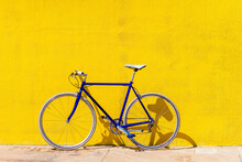 Bicycle Parked On Sidewalk By Yellow Wall During Sunny Day