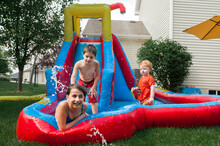 Siblings Playing In Inflatable Water Slide At Backyard