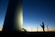 © Cavan Images - Side view of silhouette engineer looking at windmill while standing on field against clear blue sky during sunset