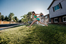 Side View Of Happy Girl Wearing Swimwear Jumping On Grassy Field Against Clear Sky In Yard