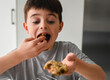 © Cavan Images - Young boy eating a freshly baked chocolate chip cookiein a kitchen