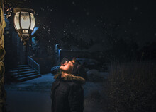 Boy Catching Snowflakes On His Tongue Beside A Light On A Snowy Night