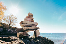 Inukshuk Rock Sculpture On A Sunny Day With Water In The Background
