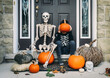 © Cavan Images - Full length of boy covering face with pumpkin while sitting by skeleton during Halloween