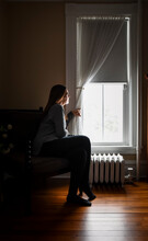 Woman Sitting In Chair Looking Out The Window In A Dark Room.