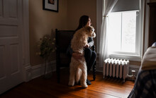Woman Hugging Dog While Sitting And Looking Out A Bedroom Window