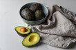 © Cavan Images - Bowl of avocados with one cut in half on a white marble countertop.