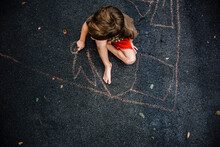 Young Boy Drawing On Driveway With Chalk, Seen From Above