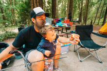 Dad And Son Roasting Marshmallows Over Propane Fire At Campsite