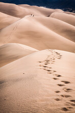A Pair Of Hikers Crosses A Dune At Great Sand Dunes National Park