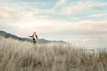 Happy Girl Wearing A Scarf Running Through Grass At A Beach