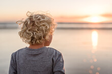 Blonde Curly Haired Boy Watching A Pink Sunrise At A Beach