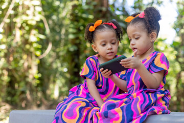 twin sisters children girls using cell phone smartphone outdoors happy