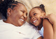 © David L/peopleimages.com - Happy, smile and family of a black grandma and child in happiness relaxing and lying on a bed at home. Senior African grandmother and little girl in joyful, love and smiling together in the bedroom