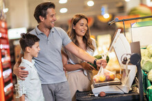 Happy Family With Child And Shopping Cart Buying Food At Grocery Store Or Supermarket