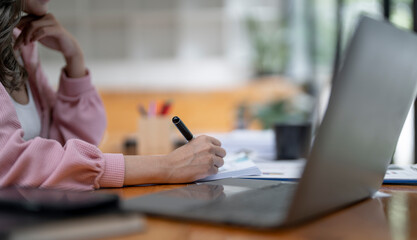 Wall Mural - Close up of businesswoman hand working on paperwork  and laptop computer at office.