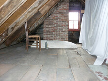 Interior Of An Attic Roof Space With A Timber Floor And Wooden Roof Trusses With A Single Old Chair Under A Window