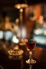 Wall Mural - A glass with cold Manhattan cocktail garnished with orange zest peel on a wooden bar counter. Bokeh lights, selective focus, small depth of field