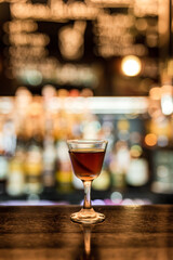 Wall Mural - A glass with cold Manhattan cocktail garnished with orange zest peel on a wooden bar counter. Bokeh lights, selective focus, small depth of field