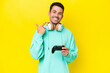 © luismolinero - Young handsome man playing with a video game controller over isolated wall giving a thumbs up gesture