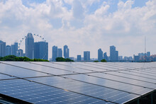Close Up View Of Solar Panels In Foreground With Modern Cityscape In The Background.