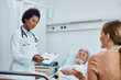 © Drazen - Black female doctor talking to senior patient's daughter during visit in hospital ward.
