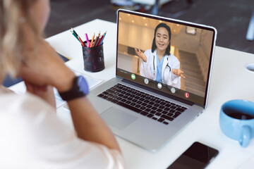 Poster - Over shoulder view of woman having laptop video call with smiling asian female doctor on screen