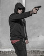 © bogdan vacarciuc - Man shooting a gun. The man's face is partially covered - he wears a hood, cap and sunglasses. Armed attack, armed robbery - concept.