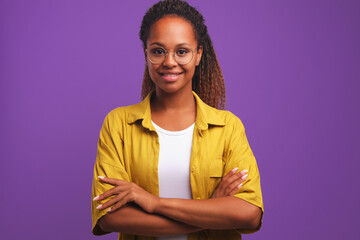 Wall Mural - Young successful positive African American woman student arms crossed in front of chest looks at camera demonstrating purposefulness and self-confidence stands on studio plain background