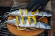 Fish (mackerel) with lemon. Chef in a black latex gloves prepares mackerel fish on a wooden cutting board, process of sprinkling with spices and salt