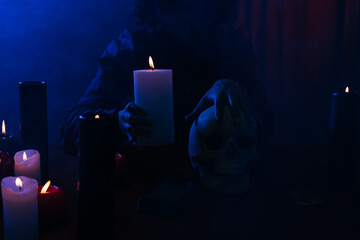 Wall Mural - cropped view of oracle with burning candle and skull during magic session in darkness near blue smoke.