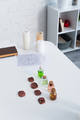 Wall Mural - clay runes and bottles with essential oils near star charts and candles on white table.
