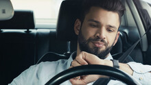 Displeased Bearded Man Driving Car And Looking At Wristwatch.