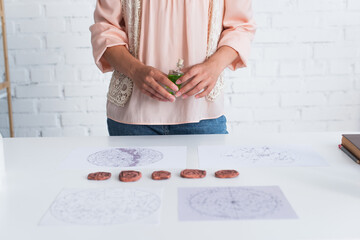 Wall Mural - partial view of fortune teller holding vial of essential oil near clay runes and astrological maps.