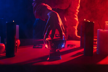 Wall Mural - cropped view of medium touching crystal ball near burning candles on dark background with smoke.