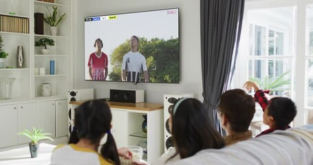 Sticker - Video of asian couple with son and daughter sitting on sofa and watching football at home