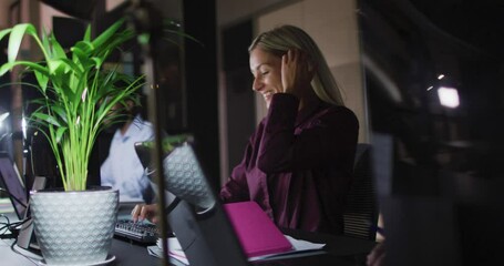 Wall Mural - video of smiling caucasian businesswoman using computer at desk with colleagues at night in office