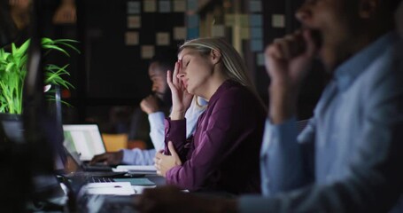 Wall Mural - video of tired caucasian busineswoman working at desk at night with colleagues in office