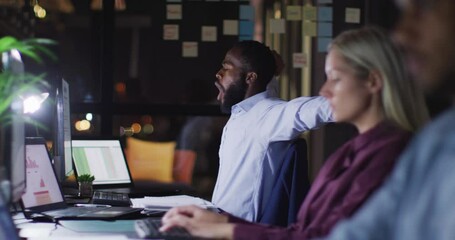 Wall Mural - video of tired african american businessman working at desk at night with colleagues in office