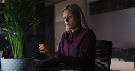 Wall Mural - video of tired caucasian businesswoman sitting at desk working at night in office