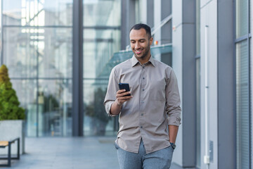 Successful young african american man walking outside office building, engineer software developer programmer smiling and happy using test app on phone, happy satisfied with result.