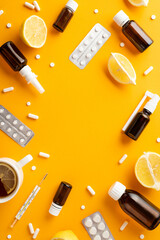 Wall Mural - Illness concept. Top view vertical photo of remedy spray and syrup bottles pills blisters thermometer cut lemon and cup of tea on isolated orange background with copyspace in the middle