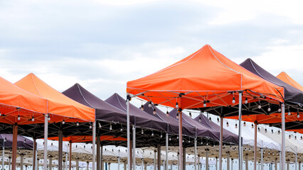 Rows of many foldable canopy tents with hanging LED light bulbs decoration for outdoors event against cloudy sky background